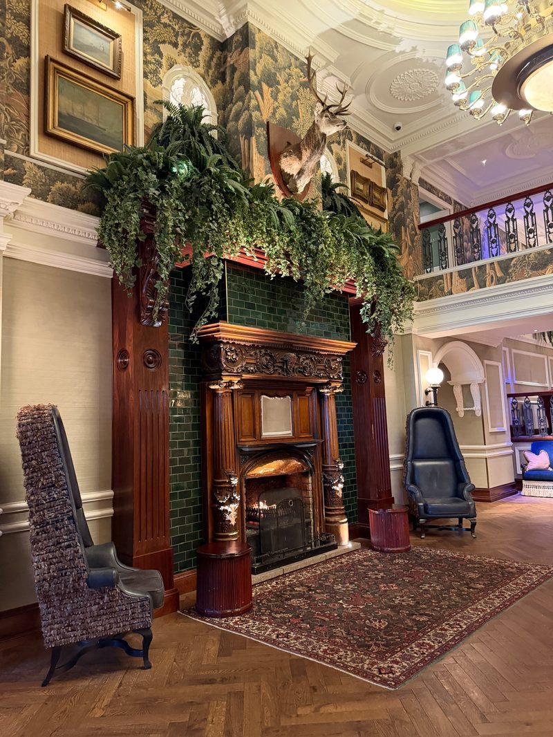 The Slieve Donard&rsquo;s grand lobby, with an ornate green-tiled fireplace, garland on the mantel, and a harp in the background.
