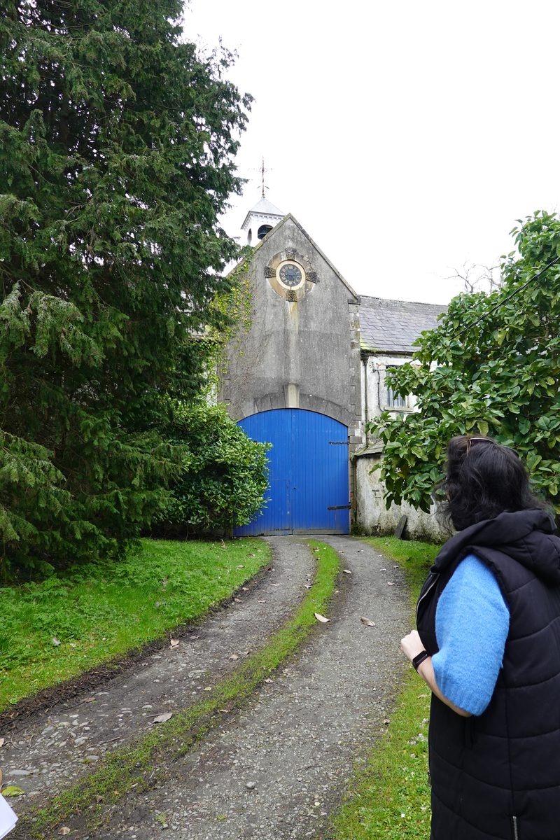 Lolly looking up a tree-lined drive toward a building with a bright blue door.