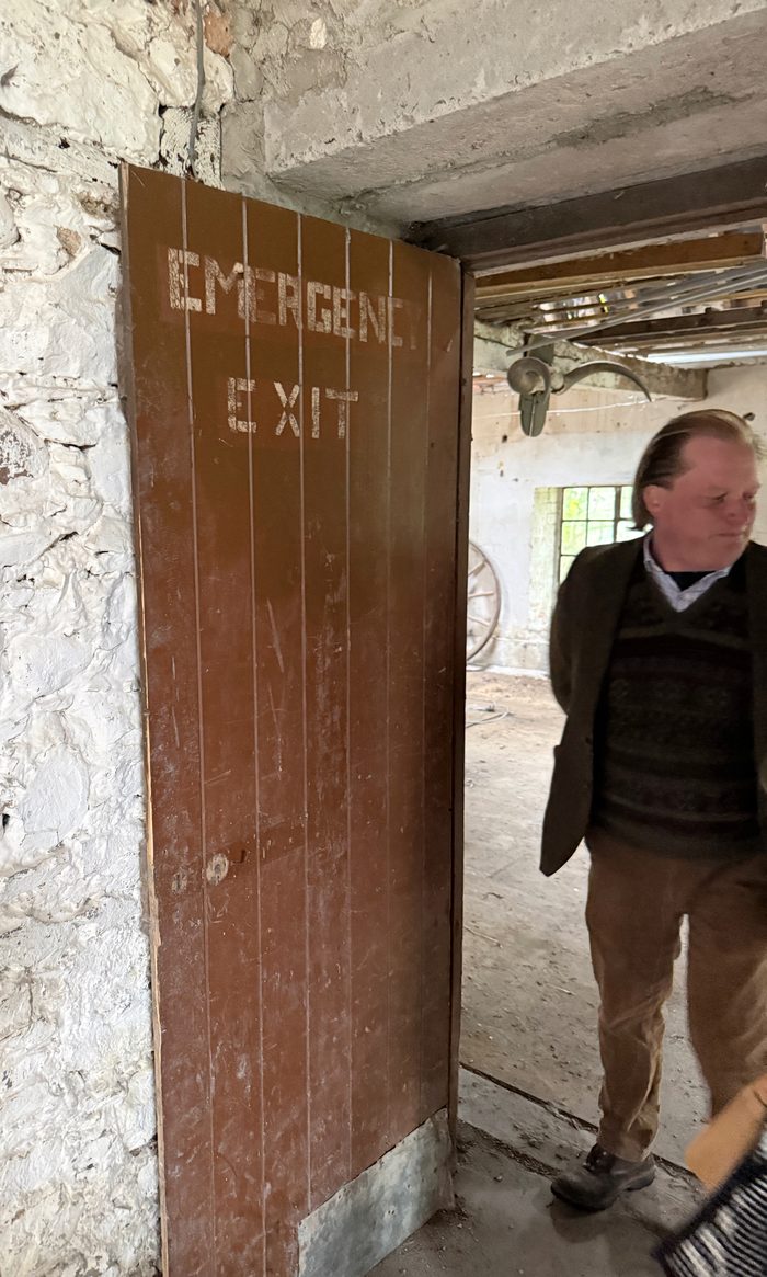 A weathered wooden door marked "Emergency Exit," propped open into one of the stable buildings.