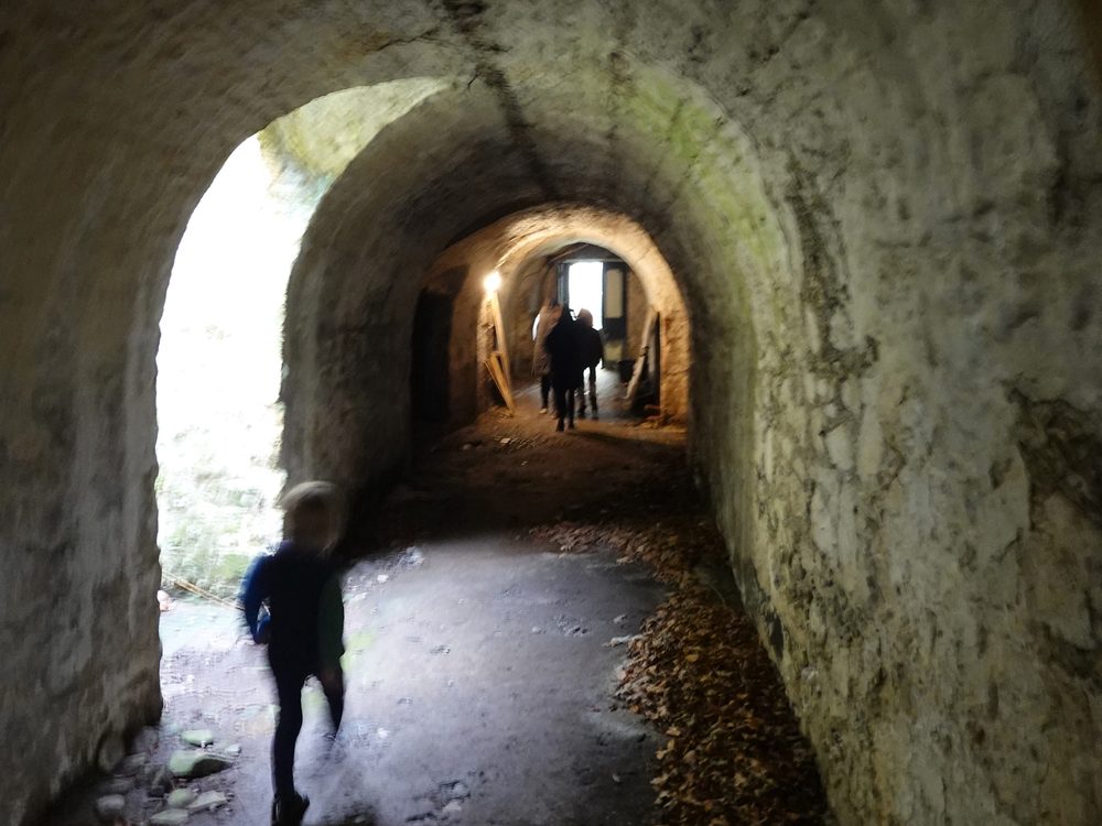 Looking down a long stone-vaulted tunnel, several archways deep, figures at different distances.
